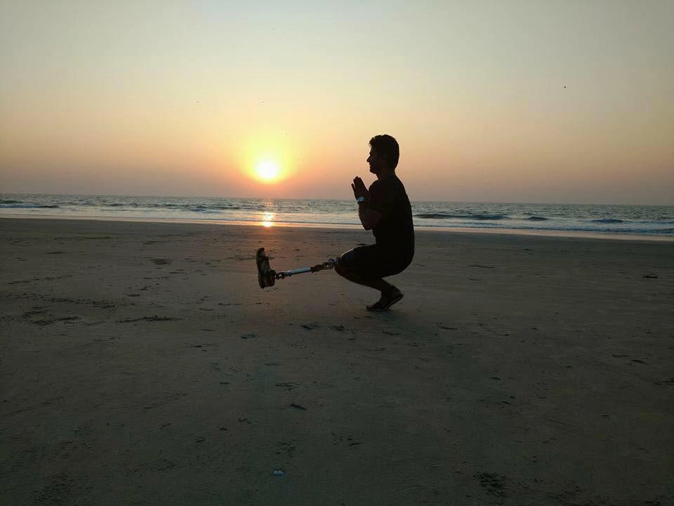 Amputee practising a yoga squat on the beach at sunrise with a running-blade prosthesis
