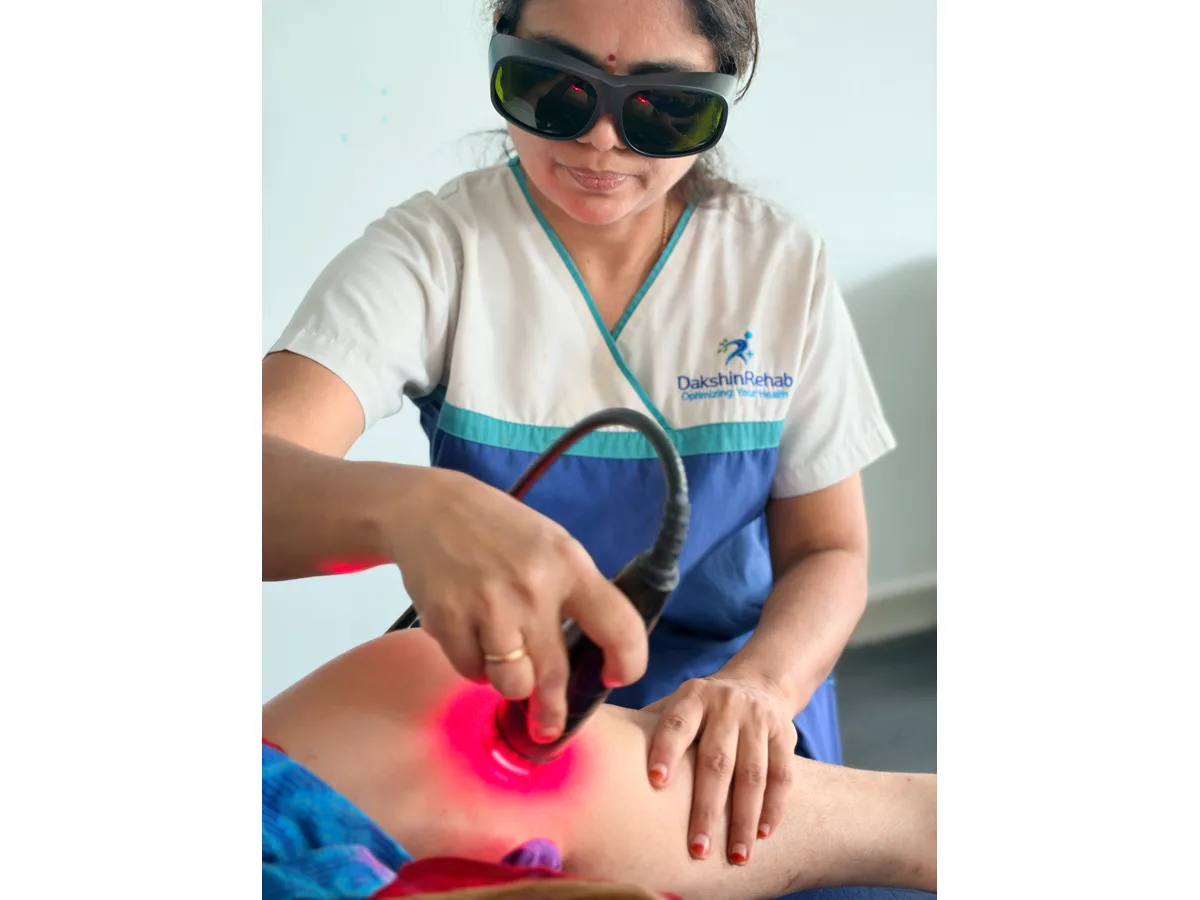 DakshinRehab physiotherapist wearing protective eyewear and applying a laser handpiece to a patient’s knee
