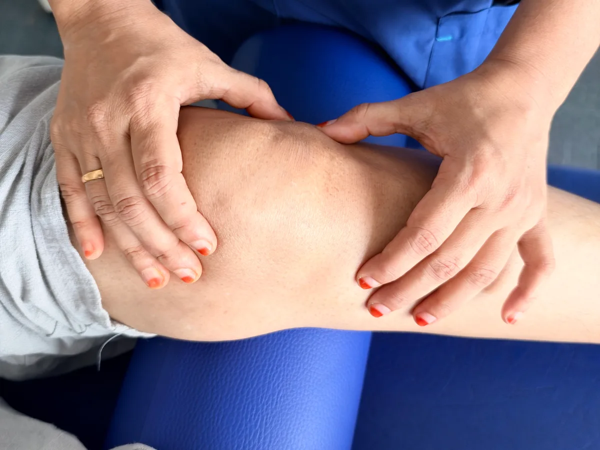 Physiotherapist examining a patient’s knee by hand